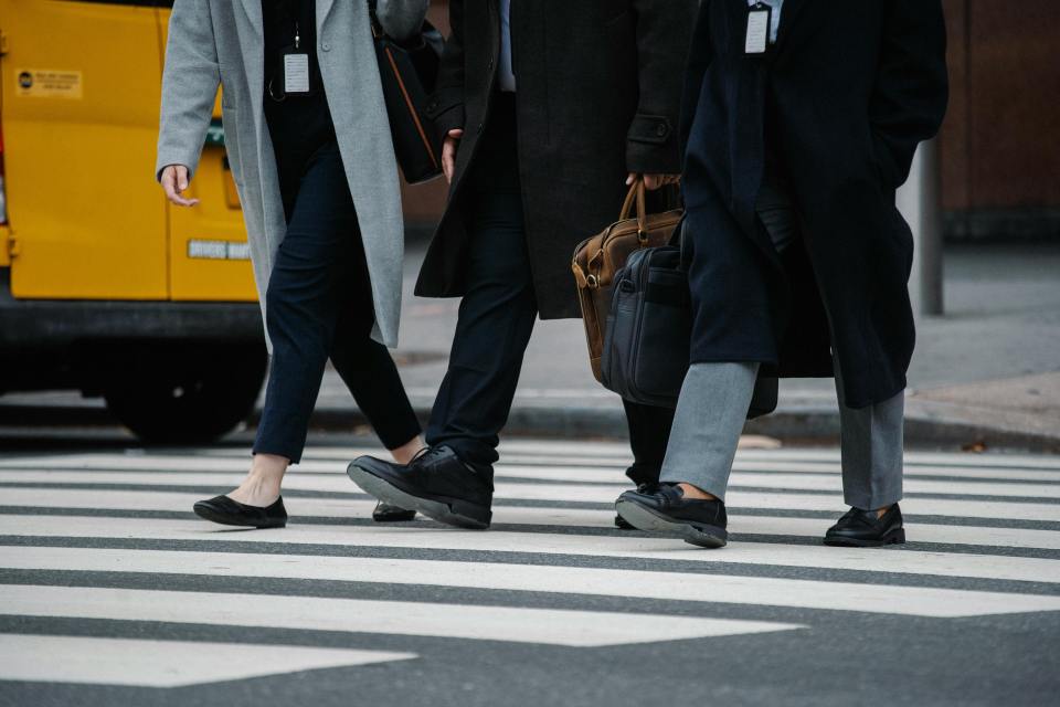 People in business attire walking across a crosswalk in the city.